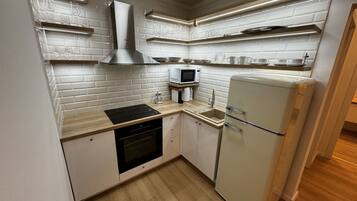 Een kleine keuken met witte bakstenen muren, een inbouwmagnetron, een roestvrijstalen afzuigkap en een koelkast in vintage stijl.