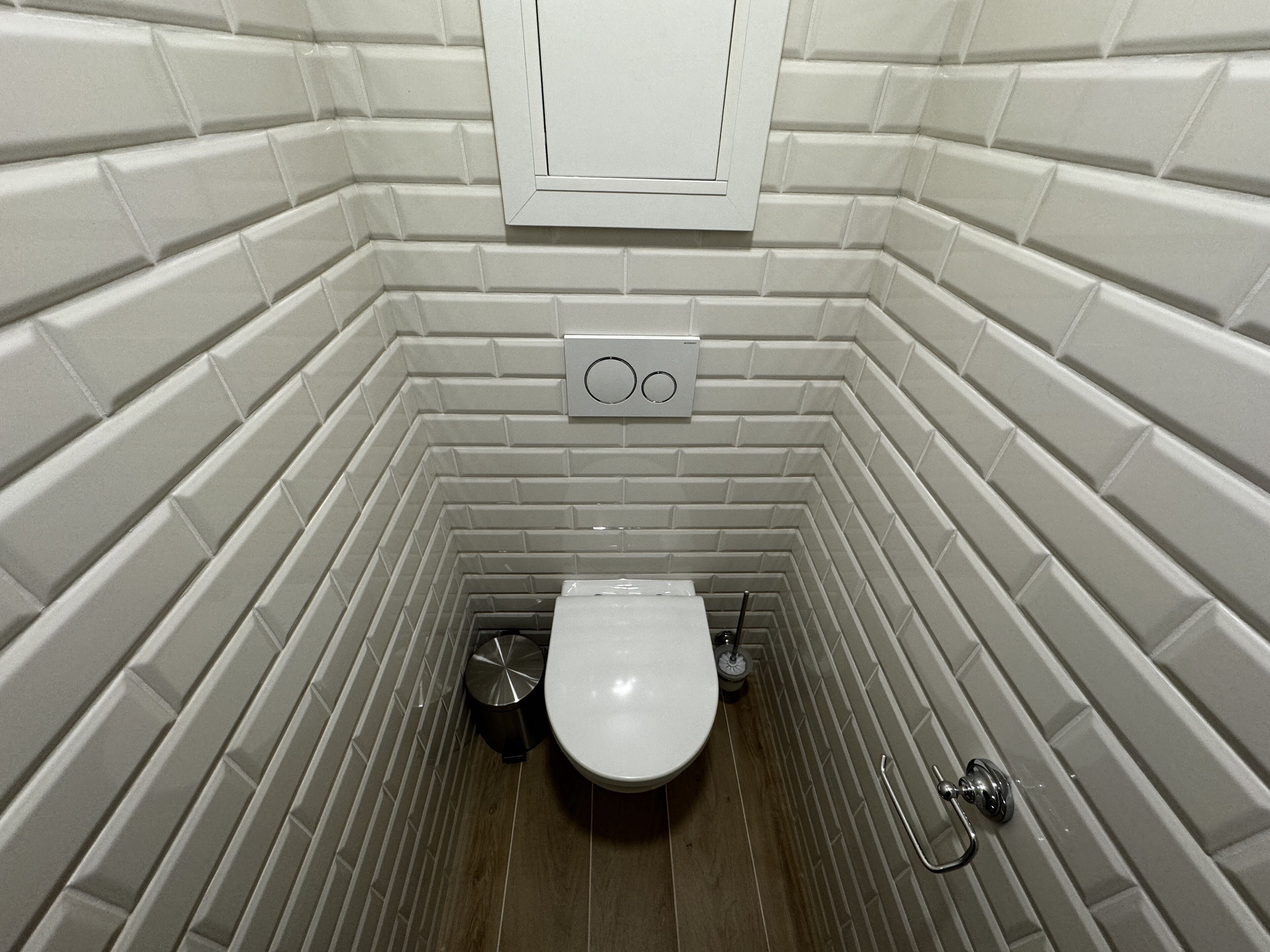 A small, narrow bathroom with white tiled walls and a wooden floor.