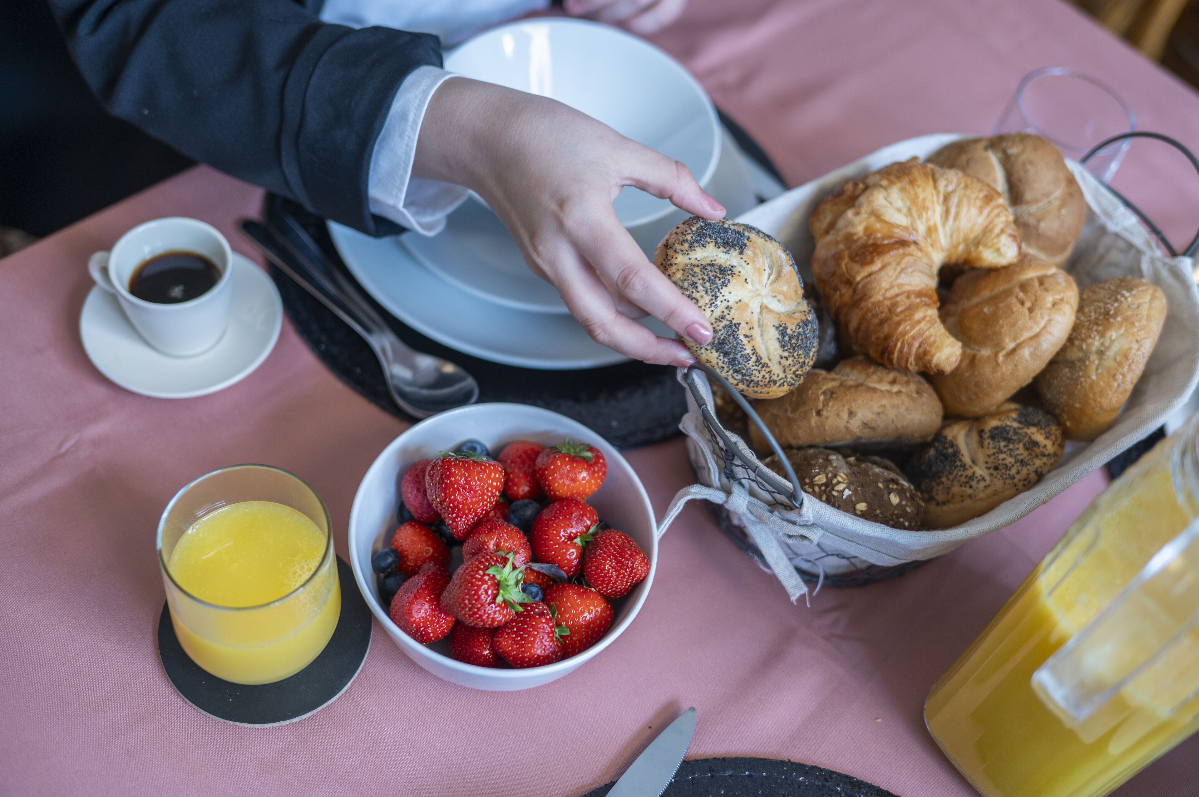 Een ontbijtsetting met croissants, aardbeien en sinaasappelsap op een roze tafelkleed.
