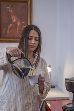 A person pouring a beverage from a kettle into a cup.