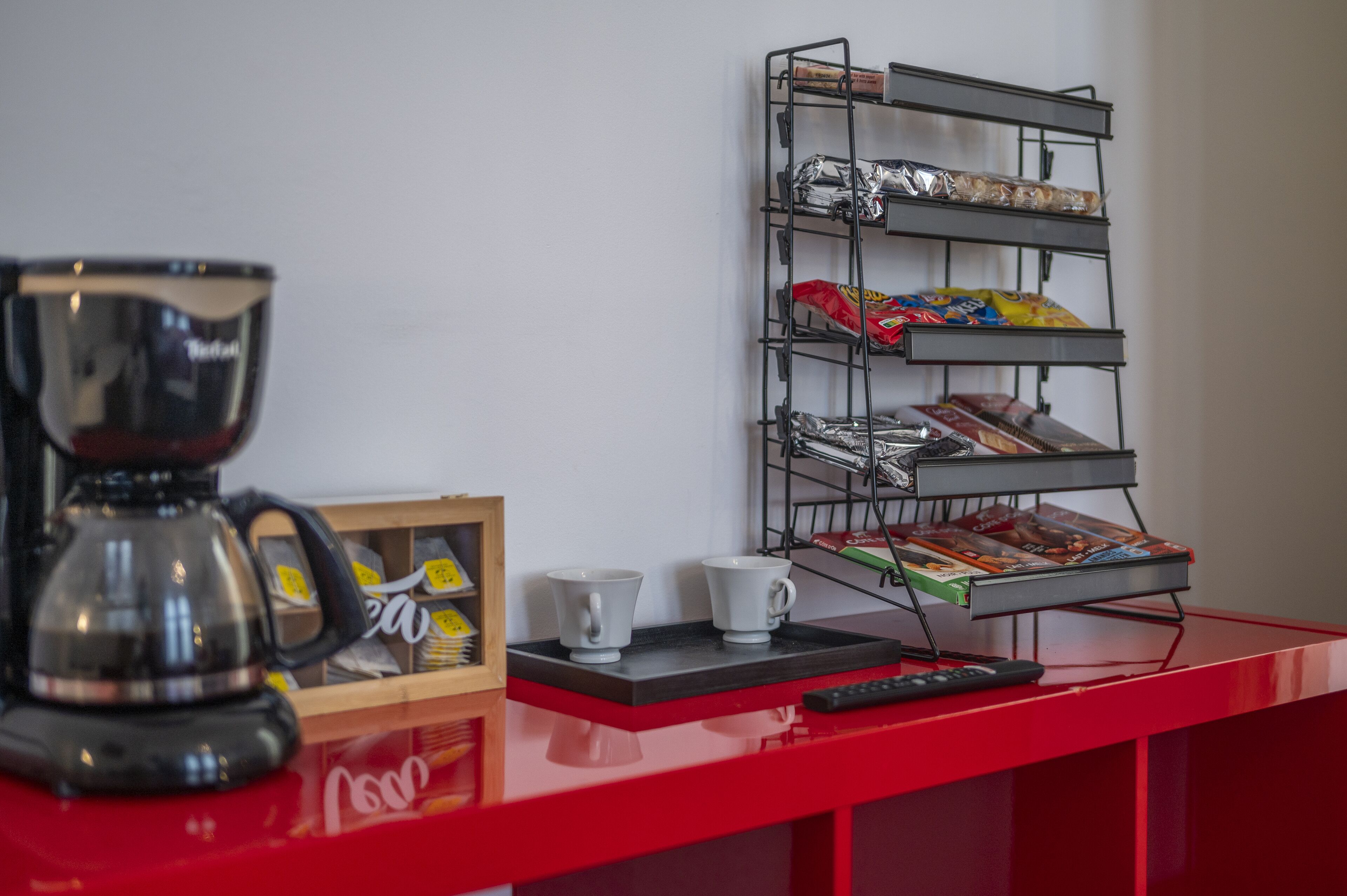 A red reception desk with a coffee maker, two white cups, a framed picture, and a magazine rack with various items.