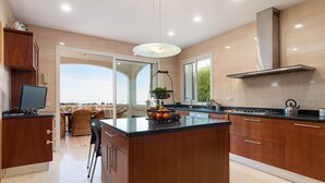 A modern kitchen with a central island, wooden cabinets, and a view to the outside. - Villa Bendinat 10: A luxurious oasis in Puerto Portals, Calvia (Calvià)
