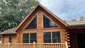Une cabane en rondins dotée d’un toit à pignon bien visible, de grandes fenêtres et d’une terrasse en bois.