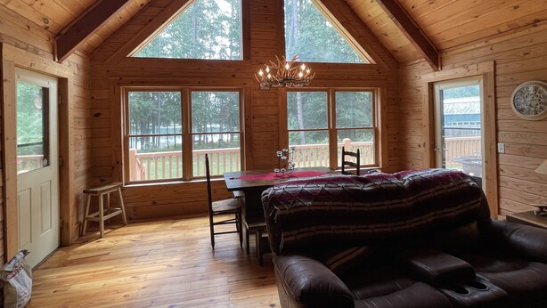 Un chalet confortable avec un plafond haut, des murs en bois et de grandes fenêtres donnant sur une terrasse et des arbres.
