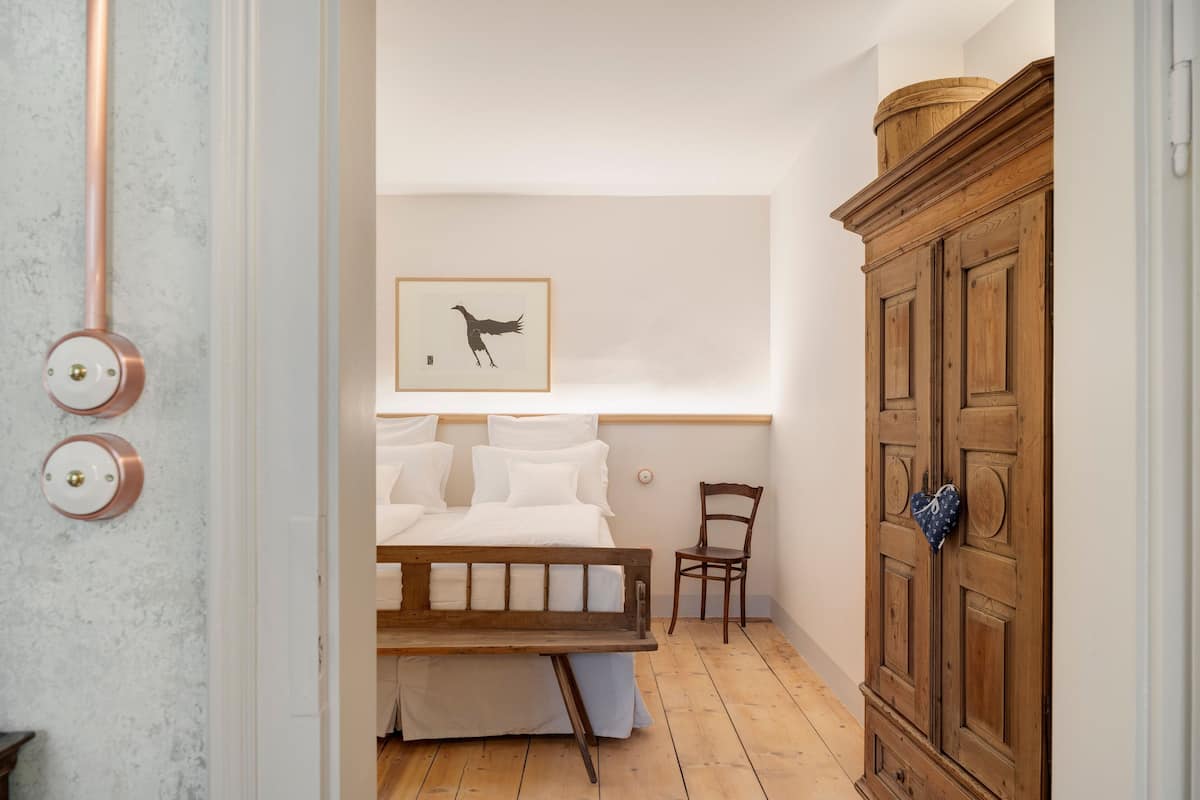 Une chambre à coucher avec un lit, une armoire en bois, un tableau encadré au mur et une chaise.