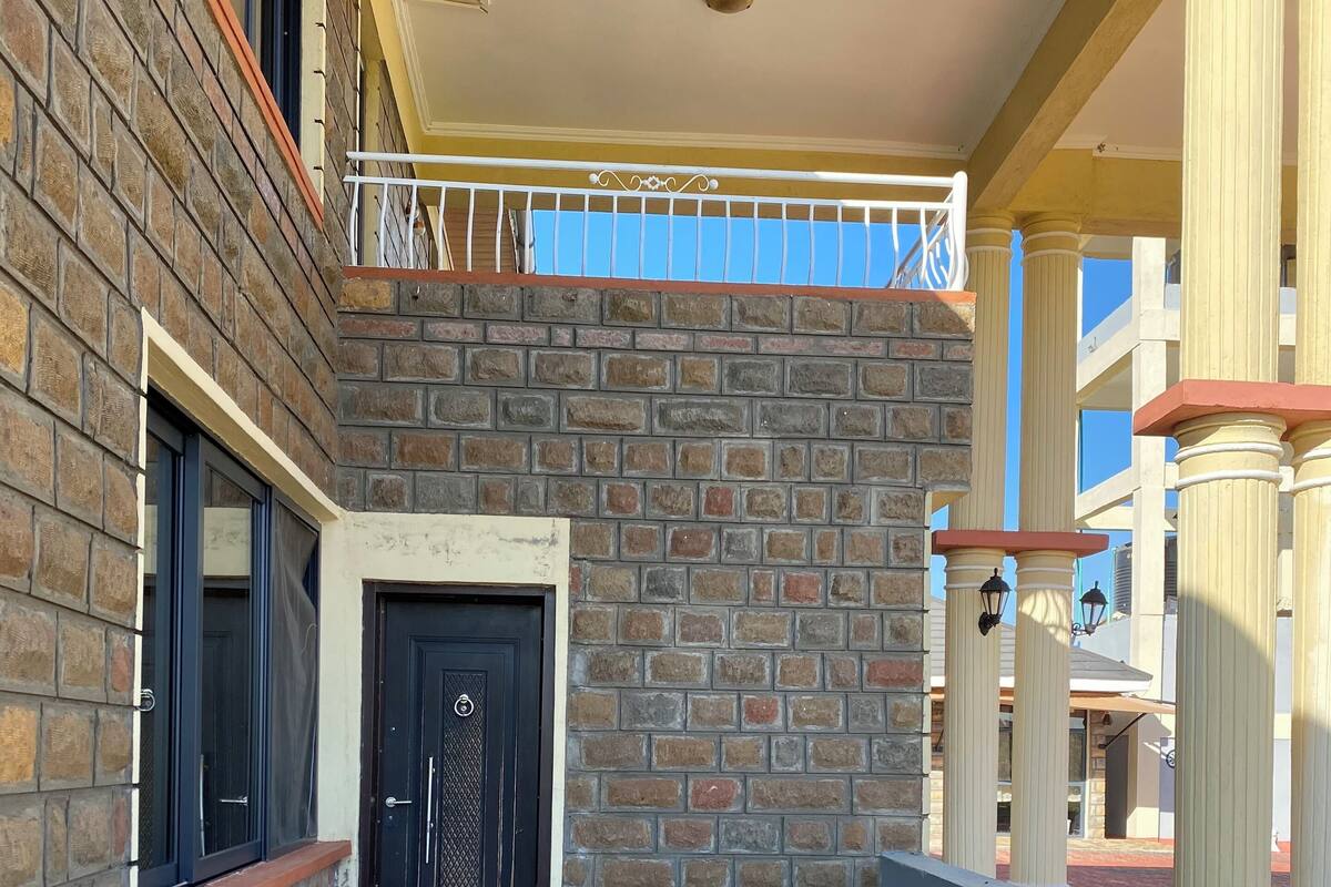 A brick building with a black door, a balcony with a railing, and columns.