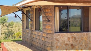 A stone building with a curved roof and large windows, featuring a stone pathway and a view of the landscape. - Mara Meguarra Sanctuary (Maasai Mara)
