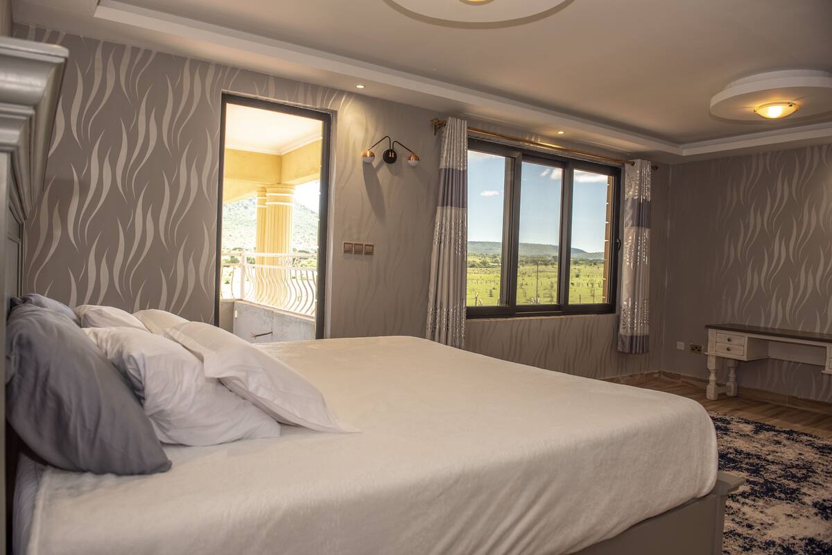 A bedroom with a large bed, a view of the outdoors, and a window with curtains.