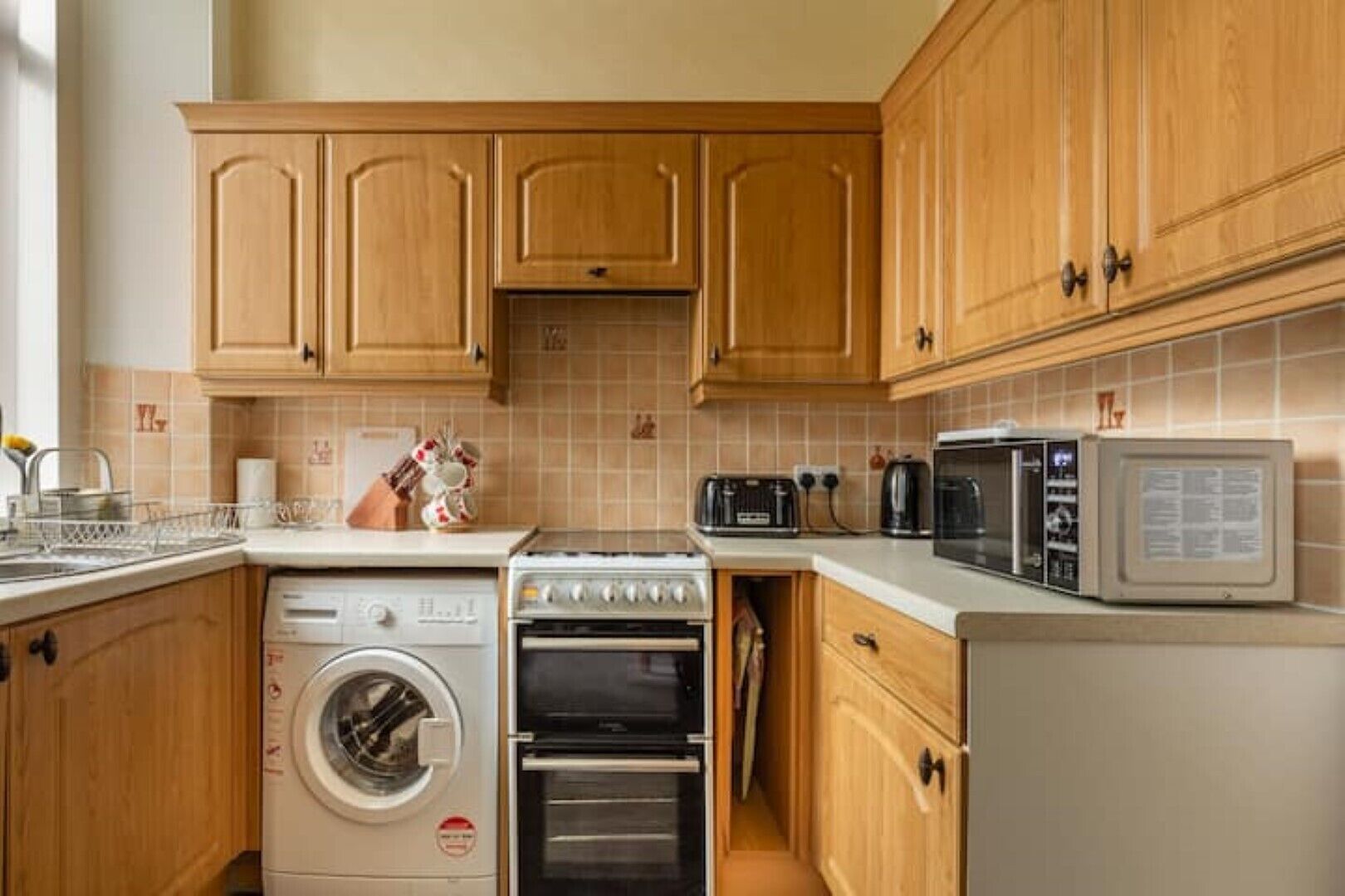 Una cocina compacta con armarios de madera, lavadora, horno, microondas y tostadora.