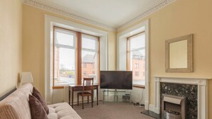 A living room with a sofa, a TV, a fireplace, and large windows.