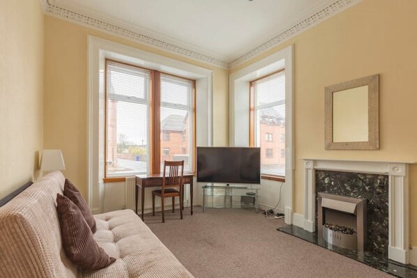 A living room with a sofa, a TV, a fireplace, and large windows.