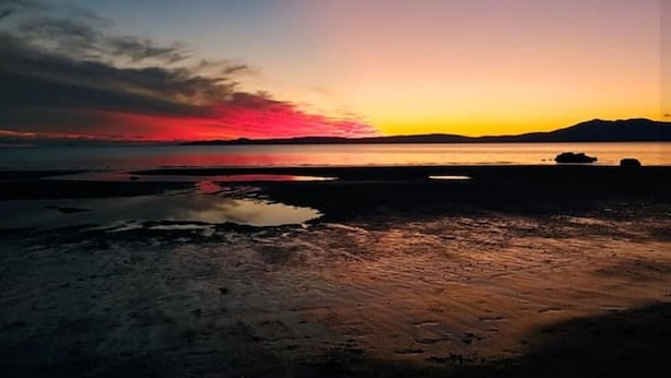 A beach at sunset with calm waters and distant mountains.