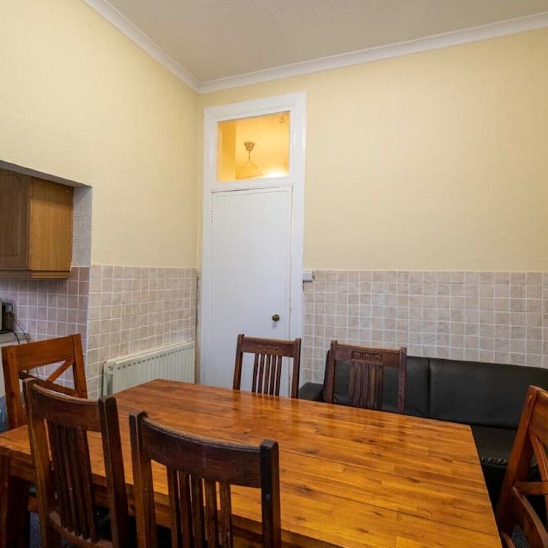 Zona pranzo con tavolo e sedie in legno, un divano nero e una porta bianca con una finestra sopra.