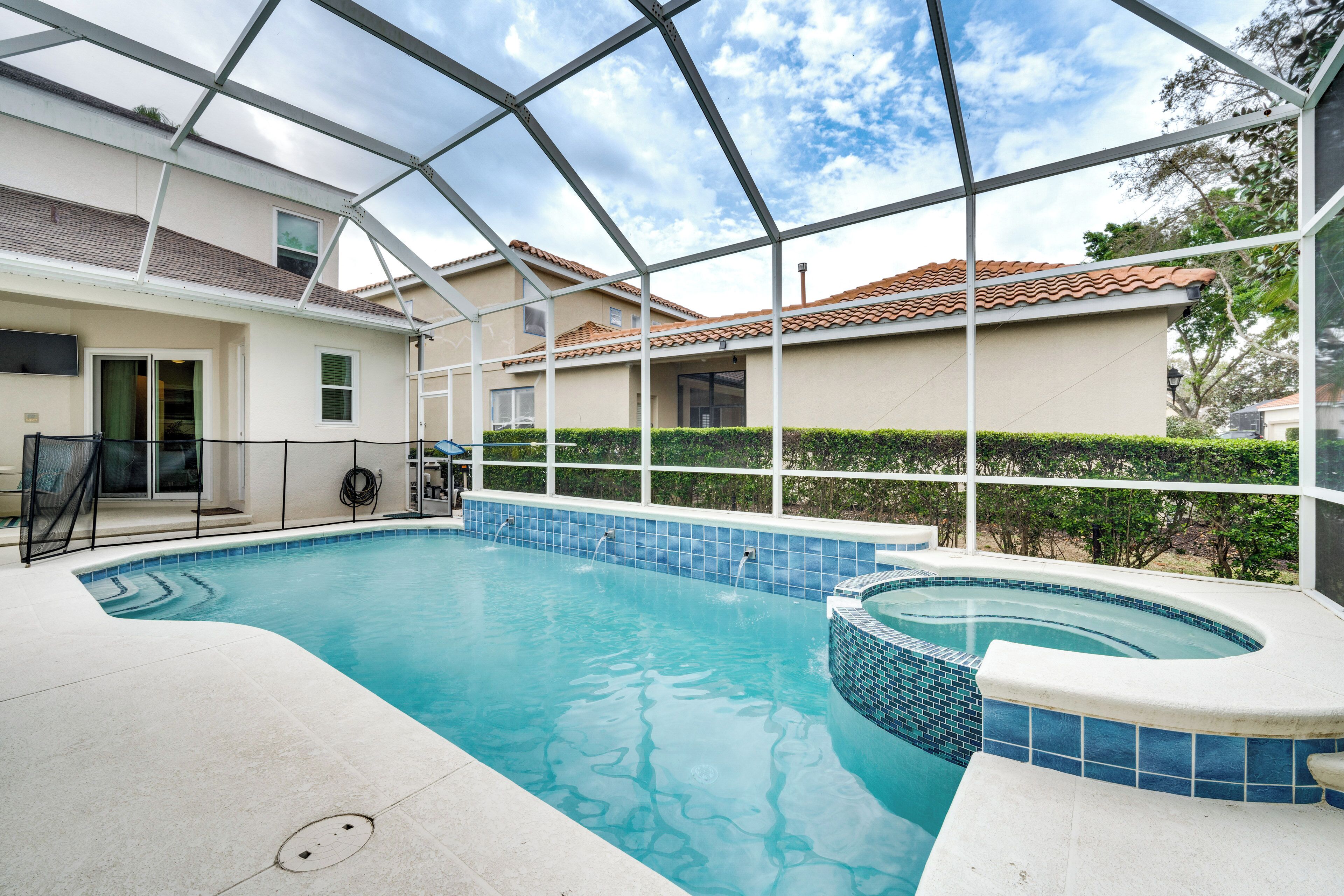 Una piscina interior con techo de cristal, rodeada por una casa con tejado de baldosas y un seto.