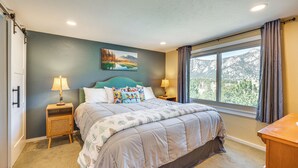 A bedroom with a large bed, two bedside tables with lamps, a window with curtains, and a painting on the wall.