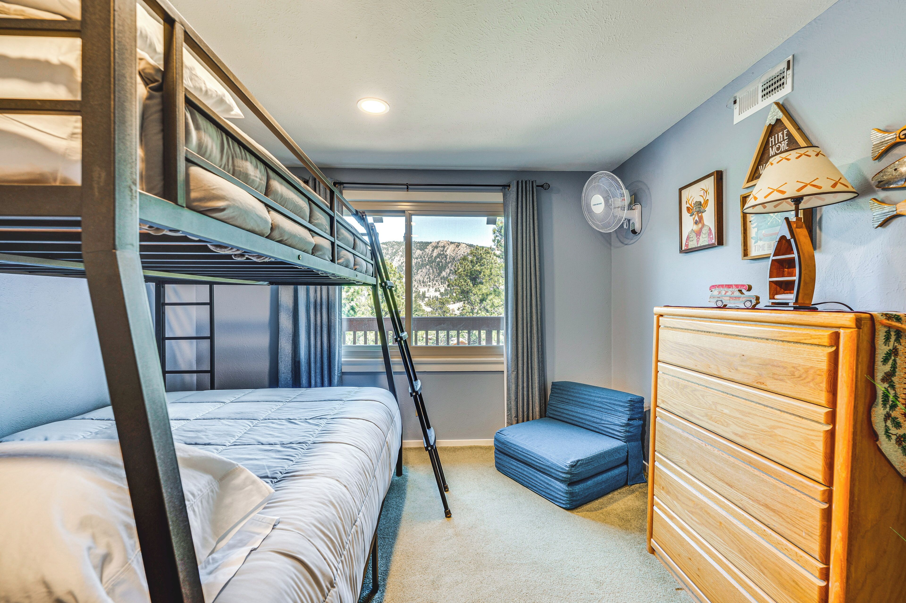 A bunk bed room with a wooden dresser, a fan, and a window with a view of a balcony.