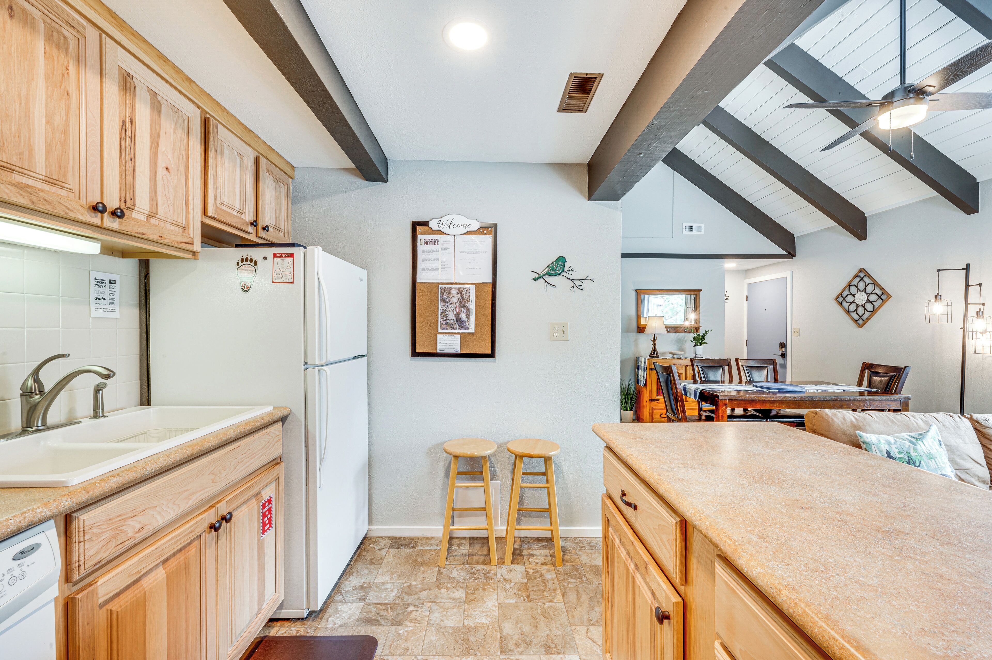Una cocina con armarios de madera, un refrigerador blanco, un tablón de anuncios y una zona de comedor con una mesa y sillas.
