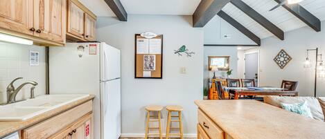 Una cocina con armarios de madera, un refrigerador blanco, un tablón de anuncios y una zona de comedor con una mesa y sillas.