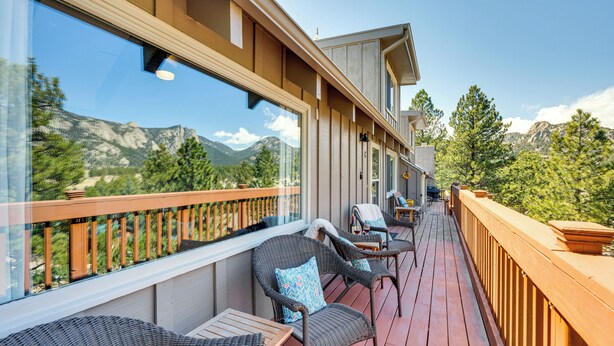 A wooden deck with wicker furniture, a glass balustrade, and a mountain view.