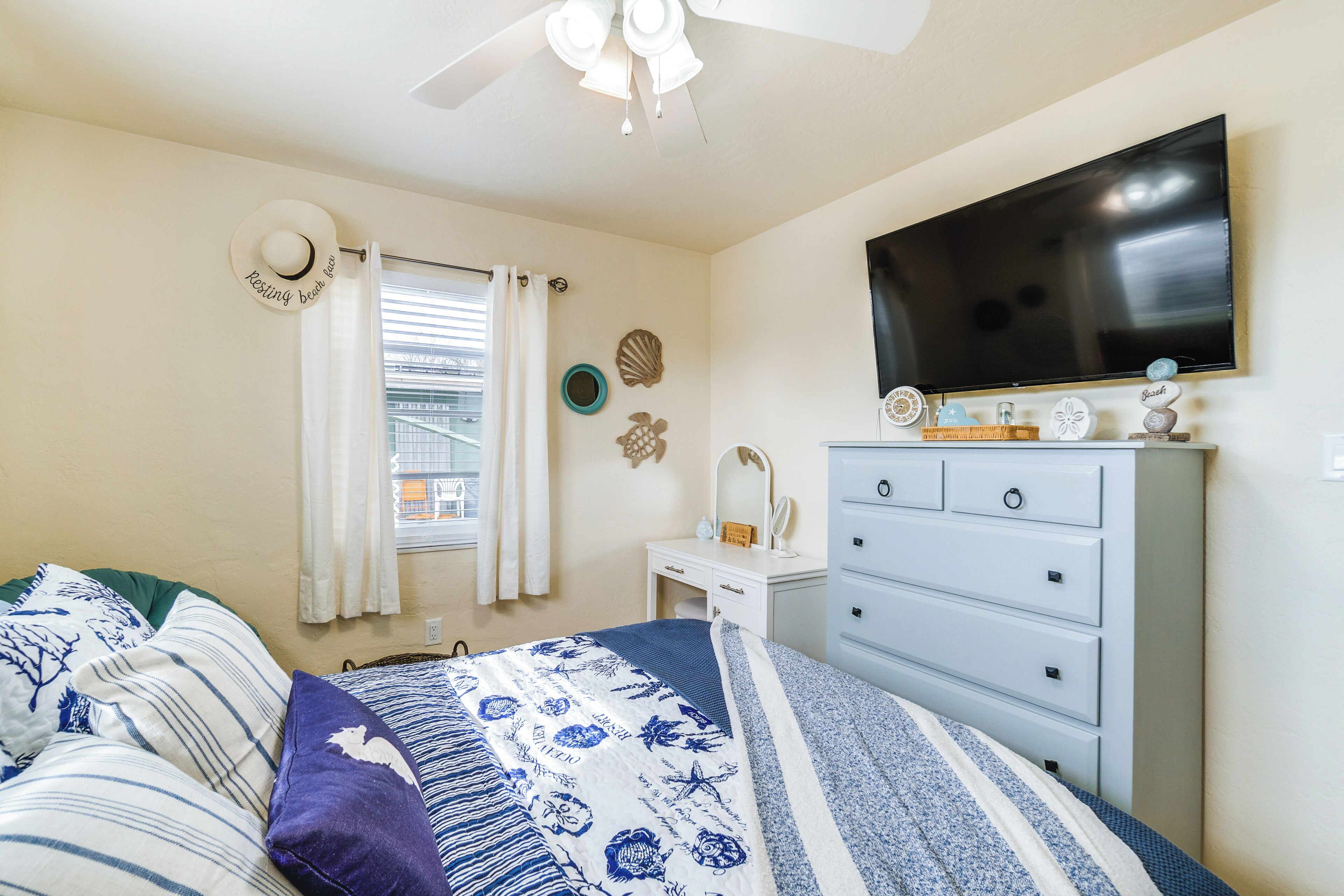 Une chambre à coucher avec un lit, une commode, un téléviseur et une fenêtre avec des rideaux.