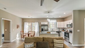 A spacious living room with a beige sofa, a dining area with a table and chairs, and a kitchen with white cabinets and appliances. - Bright Kingston Springs Home < 22 Mi to Nashville (Kingston Springs)