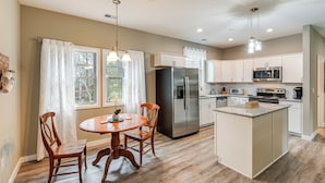 A modern kitchen with white cabinets, a stainless steel refrigerator, a microwave, and an island with a granite countertop. - Bright Kingston Springs Home < 22 Mi to Nashville (Kingston Springs)