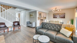 A spacious living room with a grey leather sofa, two round tables, and a staircase leading to another level. - Riverfront Champlin Townhome w/ Deck & Water View! (Champlin)