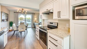 A modern kitchen with white cabinetry, stainless steel appliances, and a dining area with a table and chairs. - Riverfront Champlin Townhome w/ Deck & Water View! (Champlin)