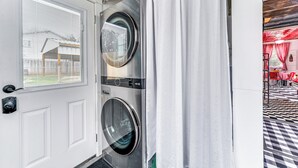 A laundry room with two front-loading washing machines, a white door, and a view of a dining area with red and white checkered tablecloths. - Fifties Diner-style Llano Home w/ Shared Fire Pit (Llano)