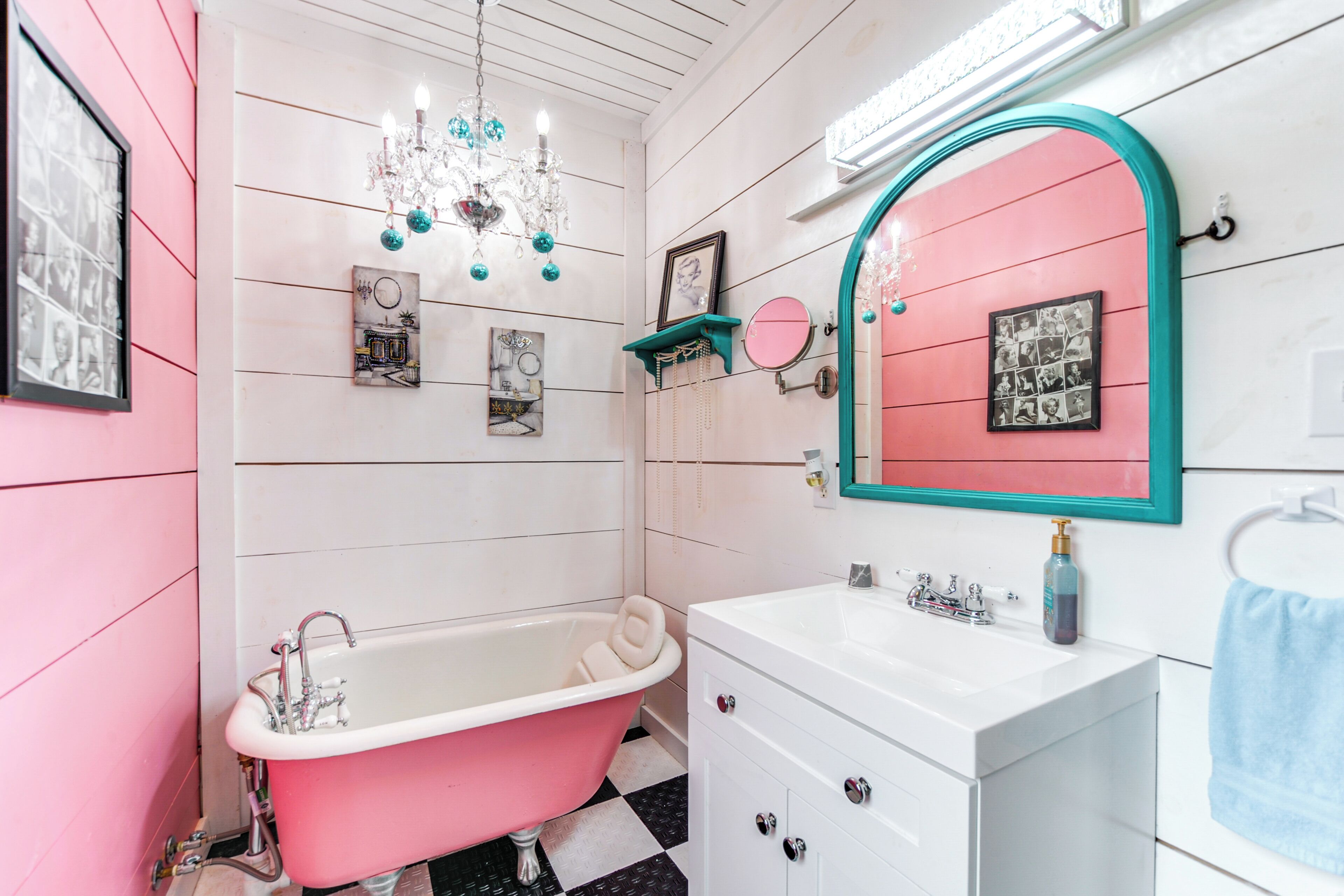 A bathroom with a pink bathtub, white vanity, and a mirror with a teal frame.