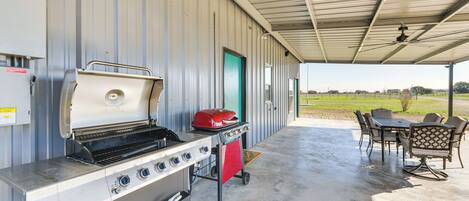 A covered outdoor area with a grill station, a table with chairs, and a view of the outdoors.