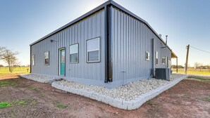 A single-story metal building with a flat roof, a green door, and a small porch area. - 4 Mi to Whitney Lake: Home on 30 Acres! (Whitney)
