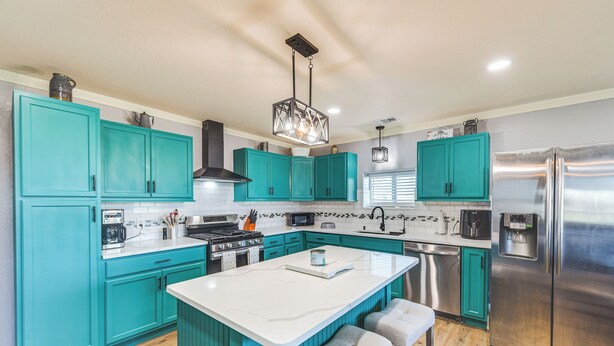 A modern kitchen with teal cabinets, a stainless steel refrigerator, and a central island with bar stools. - 4 Mi to Whitney Lake: Home on 30 Acres! (Whitney)