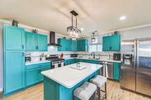 A modern kitchen with teal cabinets, a stainless steel refrigerator, and a central island with bar stools. - 4 Mi to Whitney Lake: Home on 30 Acres! (Whitney)