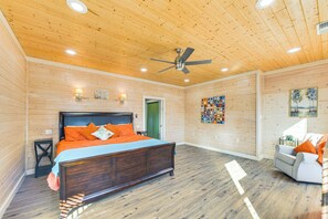 Quarto com painéis de madeira, uma cama, um ventilador de teto e uma parede decorada com obras de arte.