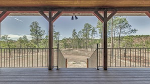 A wooden deck with a metal railing, leading to a covered area with a view of a forested landscape. - Spacious Ruidoso Home: Hike, Golf, Ski & More! (Ruidoso)