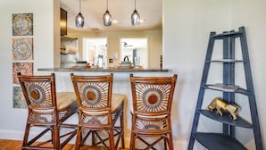 A dining area with four wicker chairs, a kitchen in the background, and a blue shelving unit with a decorative item. - Port Charlotte Vacation Rental w/ Heated Pool! (Port Charlotte)