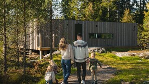 A family walking towards a modern wooden cabin in a forested area. - Grend Bø (Midt-Telemark)