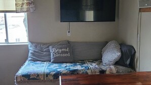 Una camera con un letto, un tavolo, una lampada a sospensione, una finestra con tende e una TV a parete.