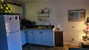 Keittiössä on jääkaappi, pesuallas ja seinälle kiinnitetty hylly, jossa on astioita.