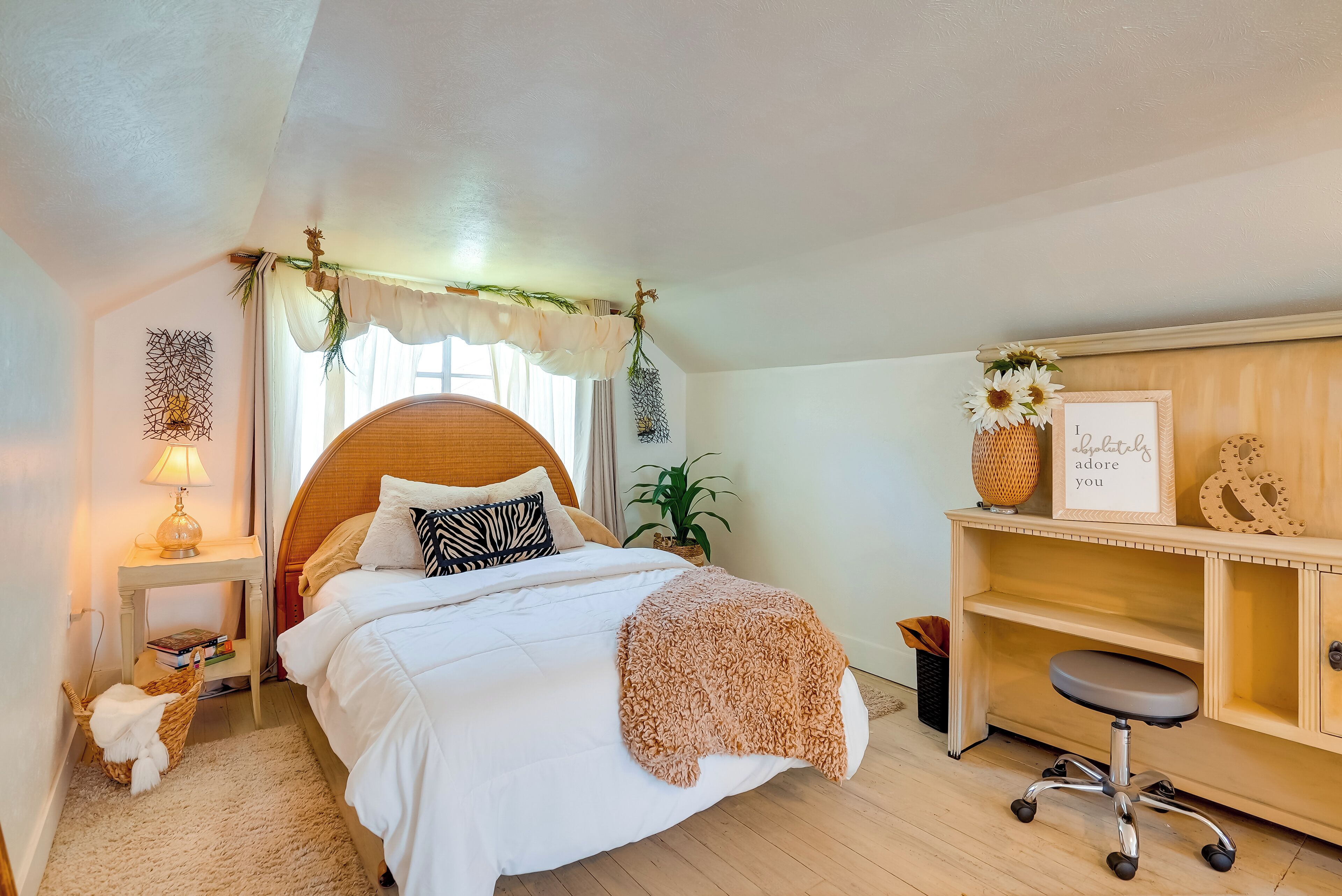 A bedroom with a bed, bedside table, lamp, and a desk with a chair.