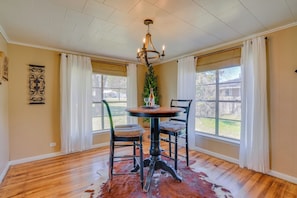 A dining room with a wooden table and chairs, a chandelier, and large windows with curtains.