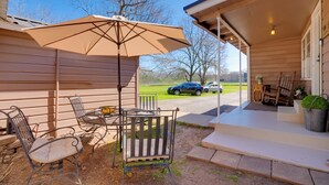 A patio with outdoor furniture and a large umbrella, a covered porch with steps, and a view of a road and cars in the background. - Rusk Retreat w/ Fire Pit, Grill & Countryside View (Rusk)