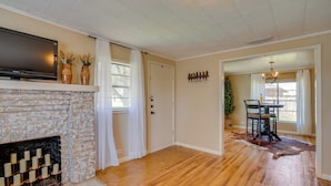 A living room with a fireplace, wooden flooring, a flat-screen TV, and a dining area with a table and chairs. - Rusk Retreat w/ Fire Pit, Grill & Countryside View (Rusk)