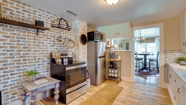 A modern kitchen with a brick wall, stainless steel appliances, and a wooden table with a plant. - Rusk Retreat w/ Fire Pit, Grill & Countryside View (Rusk)