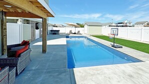 A backyard with a swimming pool, a covered patio area, and a basketball hoop. - KD300- Walk to Beach, Heated Saltwater Pool, Hot Tub (Kill Devil Hills)