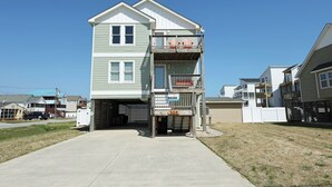 A two-story building with a balcony on the second floor, a garage entrance, and a clear sky. - KD300- Walk to Beach, Heated Saltwater Pool, Hot Tub (Kill Devil Hills)