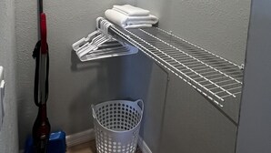 A corner of a room with a metal shelf unit, a mop, a mop bucket, and a laundry basket. - The perfect blend of comfort and convenience in our cozy studio apartment (CAPE CORAL FL)
