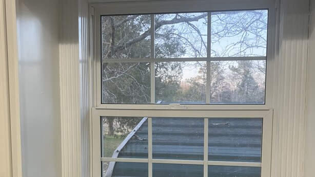 A kitchen with a double sink, a window with a view of trees and a roof, and a wooden countertop.