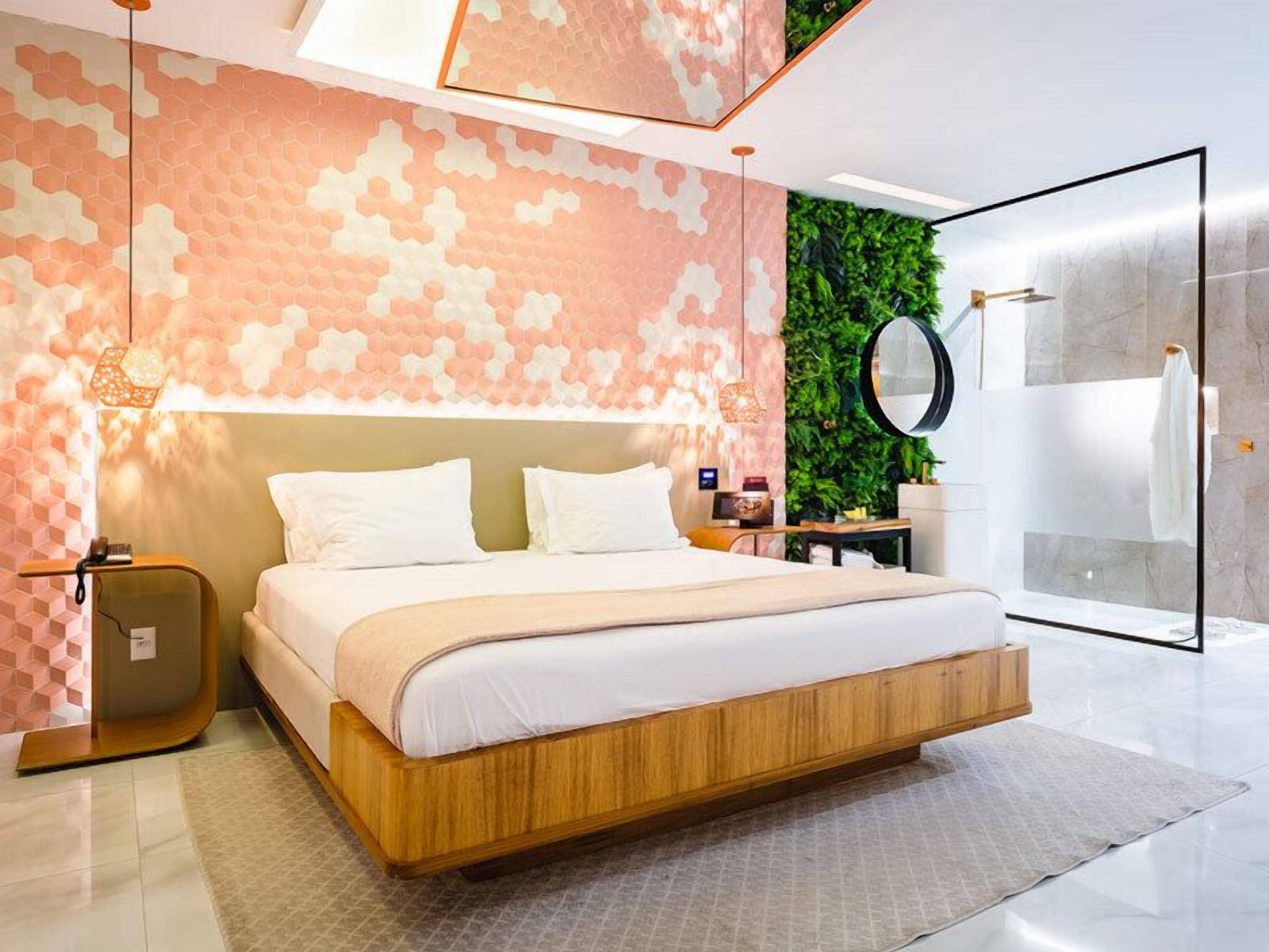 Une chambre moderne avec un grand lit, une tête de lit en bois, un mur vert orné de plantes, une douche en verre et un miroir rond.